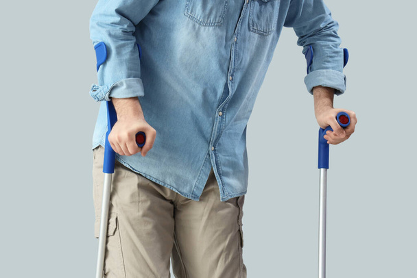 Young man with crutches on light background. National Cerebral Palsy Awareness Month - Photo, Image