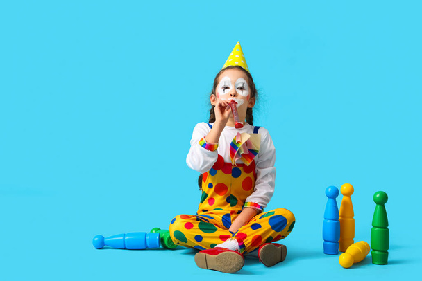 Simpatica ragazzina in costume da clown con fischietto da festa e mazze da giocoleria su sfondo blu. Festa degli sciocchi di aprile - Foto, immagini