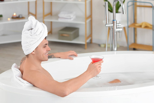 Jeune homme avec cocktail prenant bain à la maison - Photo, image