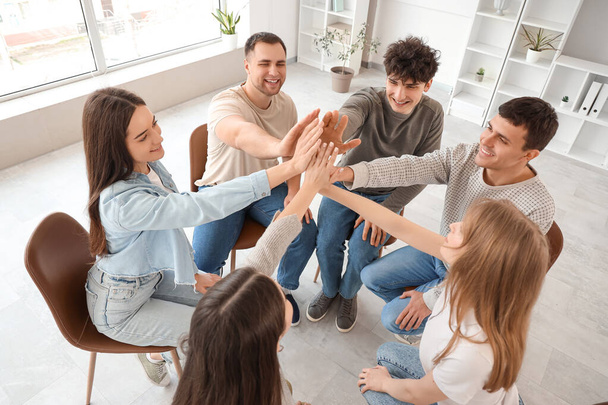 Young people putting their hands together at group therapy session - Фото, изображение