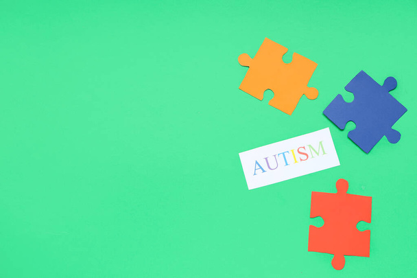 Słowo AUTISM i kolorowe puzzle na zielonym tle. Pojęcie zaburzeń autystycznych - Zdjęcie, obraz