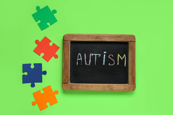 緑の背景にAUTISMとパズルという単語が付いたブラックボード. 自閉症障害コンセプト - 写真・画像