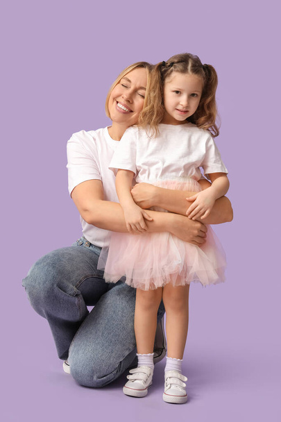 Glückliche Mutter umarmt ihre Tochter auf fliederfarbenem Hintergrund. Muttertag - Foto, Bild