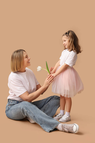 Mała dziewczynka daje kwiaty matce na beżowym tle. Dzień Matki - Zdjęcie, obraz