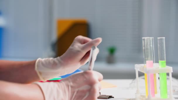 Medizinisches Labor, junge Ärztin in Handschuhen schreibt Beobachtungen von Reagenzien und Substanzen im Reagenzglas in einem Notizbuch auf, während sie im Krankenhausbüro sitzt, Nahaufnahme - Filmmaterial, Video