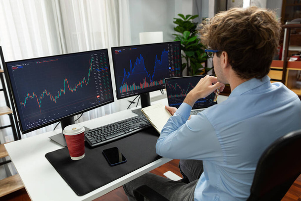 Working young business trader looking on laptop on screens, holding notepad and pen on market stock graph investing in real time at office on panorama, analyzing dynamic investment concept. Gusher. - Photo, Image