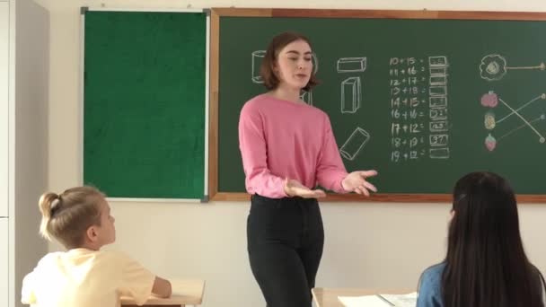 Valkoihoinen opettaja pyytää vapaaehtoista, kun aasialainen tyttö kävelee luokan edessä luottavaisena. Fiksu opiskelija nosti kätensä ja vastata kysymykseen, kun opettaja taputtaa kädet kannustaa. Pedagogiikka. - Materiaali, video