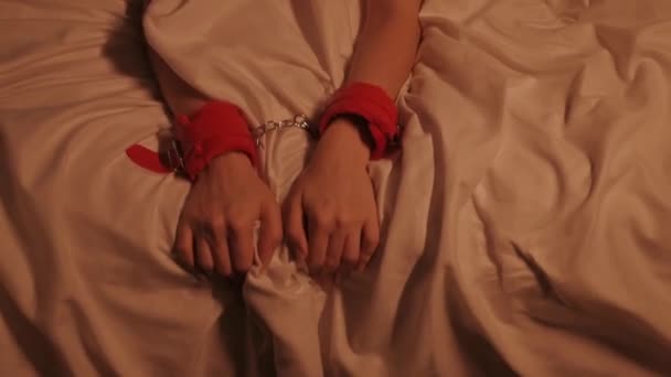 handcuffed hands of female girl woman submissive in BDSM handcuffs in hard sex and orgasm squeeze a white sheet on the bed at night - Footage, Video