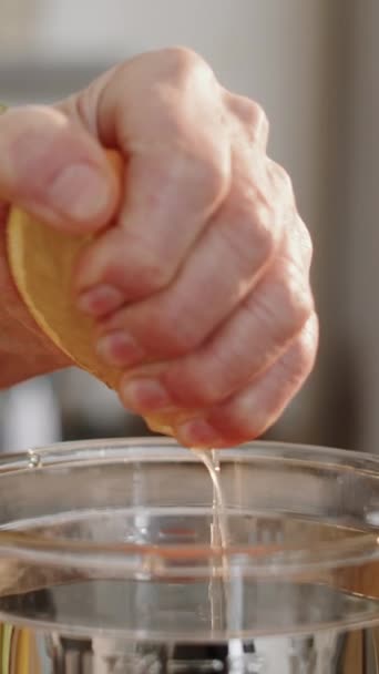 Primo piano verticale della mano rugosa femminile irriconoscibile che stringe limone fresco nel frullatore mentre prepara una sana bevanda vitaminica al mattino - Filmati, video