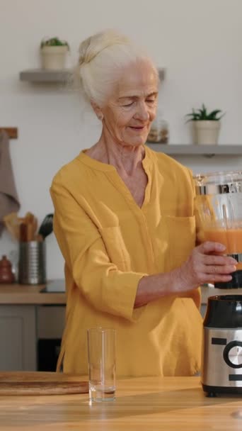 Mutfak masasının yanında duran ve blender 'dan taze vitamin içeceği döken beyaz bir kadının orta boy dikey fotoğrafı. - Video, Çekim