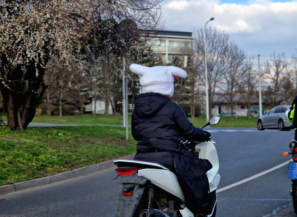 Мотоцикл водит мужчина или женщина в шлеме с капюшоном в форме зайца. уши и белый плюшевый чехол. смешное дополнение к городскому движению - Фото, изображение