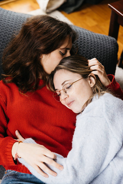 Lesbian couple lying on the living room floor, embracing and caressing each other. Young female couple sharing a moment of tenderness and affection in an intimate and cozy atmosphere. - Photo, Image
