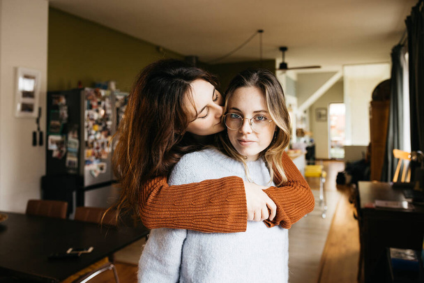 Tierno retrato de una joven hermosa pareja de lesbianas abrazándose en la acogedora sala de estar de su casa. - Foto, imagen