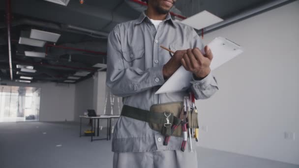 Inclinación hacia arriba retrato de trabajador de la obra de construcción afroamericano en uniforme sosteniendo plano - Metraje, vídeo