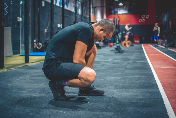 Vista lateral del deportista en forma atando cordones de zapatos, listo para entrenar en el gimnasio - Foto, imagen