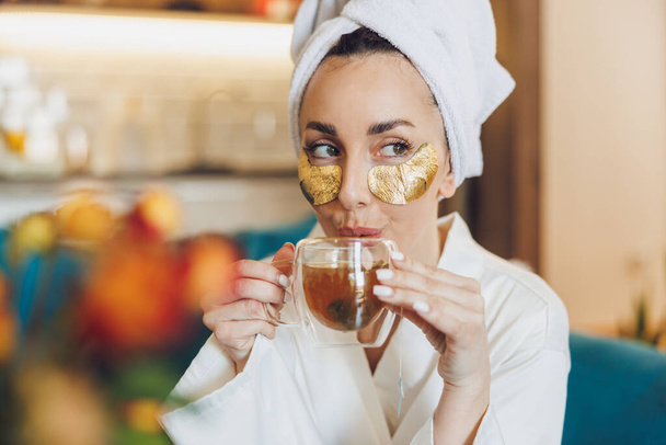 Atraktivní žena s péčí o pleť pod očima náplasti těší ranní čaj a relaxaci u ní doma. - Fotografie, Obrázek