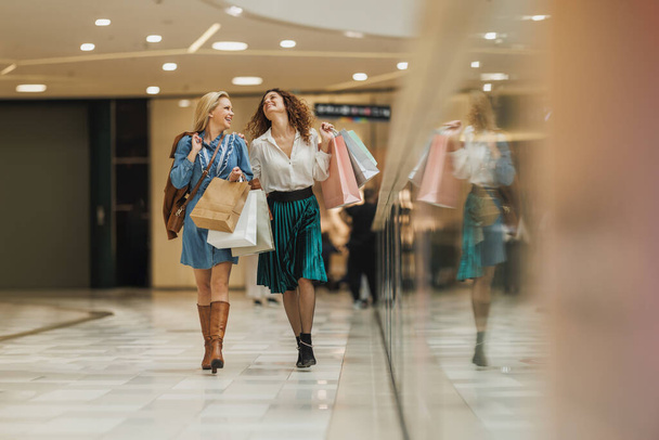 Постріл двох привабливих подруг, посміхаючись під час прогулянки з сумками в міському торговому центрі протягом дня. - Фото, зображення