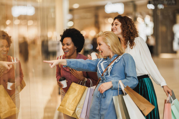 Atrakcyjna kobieta wskazująca na coś, ciesząca się dniem zakupów z najlepszymi przyjaciółmi w centrum handlowym.. - Zdjęcie, obraz