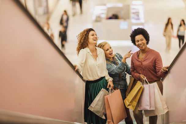 Una bella donna punta verso qualcosa mentre si gode una giornata di shopping con i suoi migliori amici nel centro commerciale della città. - Foto, immagini