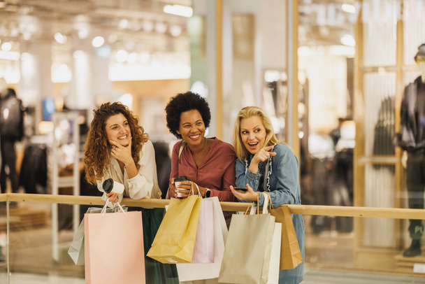 Снимок привлекательной женщины, указывающей на что-то во время отдыха со своими лучшими друзьями во время шоппинга в торговом центре. - Фото, изображение