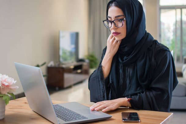 Mujer árabe pensativo o preocupado en abaya utilizando el ordenador portátil en casa - Foto, imagen
