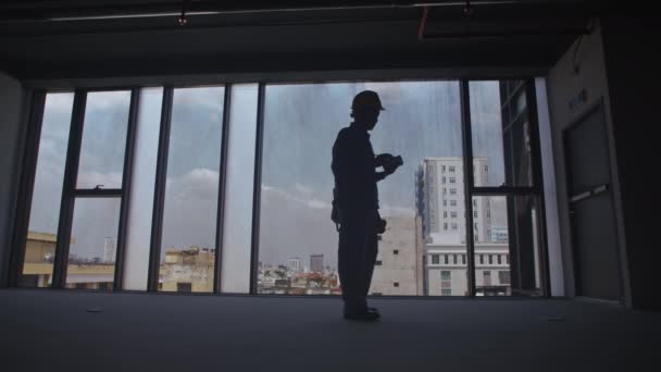 Lange Aufnahme der Silhouette eines Bauarbeiters, der Raumgrößen misst - Filmmaterial, Video