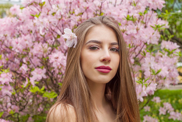 自然なメイクと屋外の花の公園で健康な長い茶色の髪を持つ完璧な若い女性. 自然な女性の美しさの肖像画 - 写真・画像