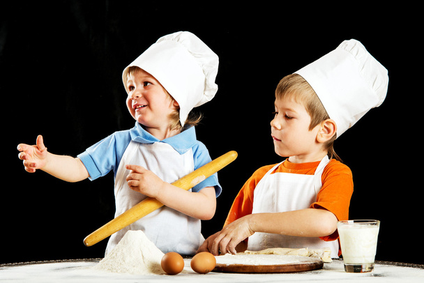Dwa mały chłopiec robienia pizzy czy makaronów ciasta. Na czarnym tle. - Zdjęcie, obraz