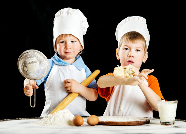 Dwa mały chłopiec robienia pizzy czy makaronów ciasta. Na czarnym tle - Zdjęcie, obraz