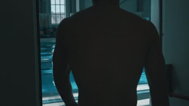 Medium rear follow shot of male swimmer walking out of changing room, rotating arms, warming up wrists, greeting coach, who is showing practice plan on smartphone and setting goals for workout - Footage, Video