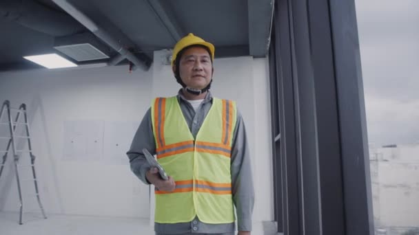 Pan portret azjatyckiego brygadzisty w mundurze uśmiecha się do kamery na placu budowy, przestrzeń kopiowania - Materiał filmowy, wideo