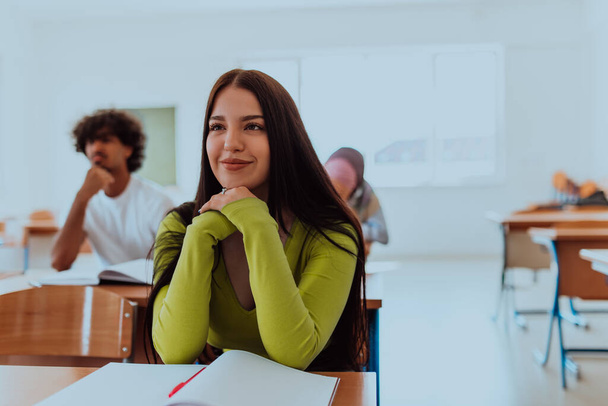 Studentka s vřelým úsměvem pozorně poslouchá přednášku v univerzitní třídě, její zelená košile popírá její nadšení pro učení.  - Fotografie, Obrázek
