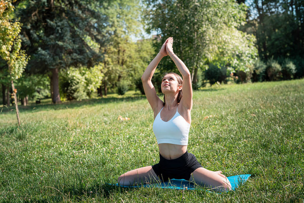 Štíhlá hezká žena cvičí relaxační jógu nebo pilates v přírodě. Čas na sport v létě ráno v parku - Fotografie, Obrázek