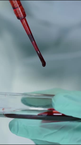 Primo piano verticale dello scienziato irriconoscibile con pipetta mentre gocciola liquido rosso denso sulla capsula di Petri, conducendo esperimenti in laboratorio - Filmati, video