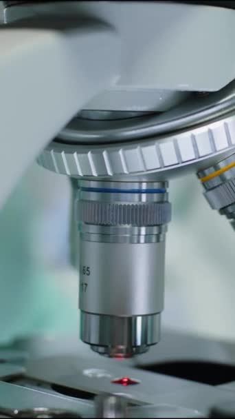 Primer plano vertical del microbiólogo irreconocible en guantes lentes objetivo giratorias en el microscopio mientras se investiga en laboratorio - Metraje, vídeo