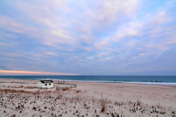 La scena tranquilla di una spiaggia all'alba, con una piccola cabina, cielo colorato e vegetazione costiera che crea un'atmosfera di pace e serenità.. - Foto, immagini