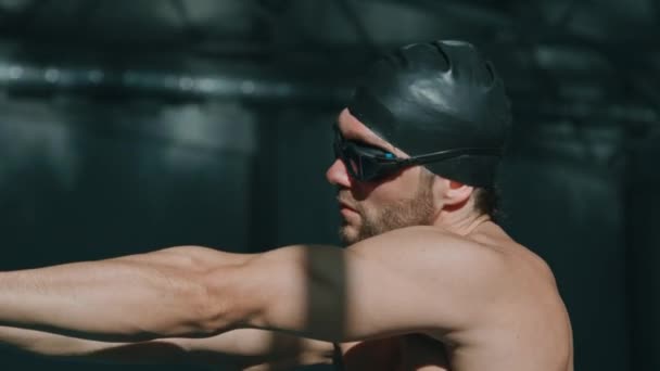 Μέτριο κοντινό πλάνο πλαϊνό πλάνο του νεαρού αθλητή τριάθλου σε γυαλιά κολύμβησης, λαστιχένιο καπάκι κάμψης κεφαλής, περιστρεφόμενους ώμους, τεντωμένους βραχίονες, ενώ ετοιμάζεται για προπόνηση στην πισίνα - Πλάνα, βίντεο