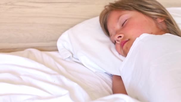 Маленькая девочка с длинными волосами мирно спит в удобной кровати на белой подушке по утрам. Закрыть замедленный зум в клипе. Идеально подходит для проектов, связанных с семьей, детством или - Кадры, видео