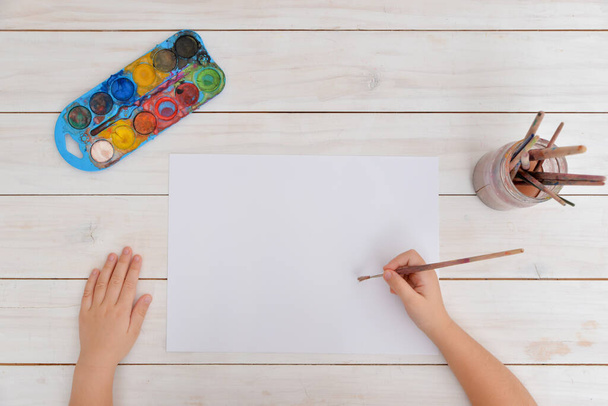 Руки используют кисть для акварельной живописи на чистой бумаге. Концепция творчества, искусства, детства, воображения и художественного выражения - Фото, изображение