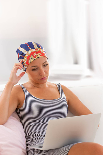 Driekwart lengte jonge vrouw dragen hoofddoek met behulp van laptop computer - Foto, afbeelding