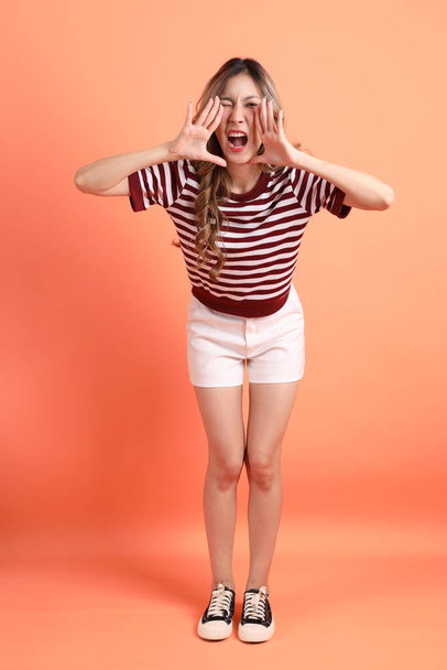 Молодая азиатка в повседневной одежде с жестом крика на оранжевом фоне  - Фото, изображение