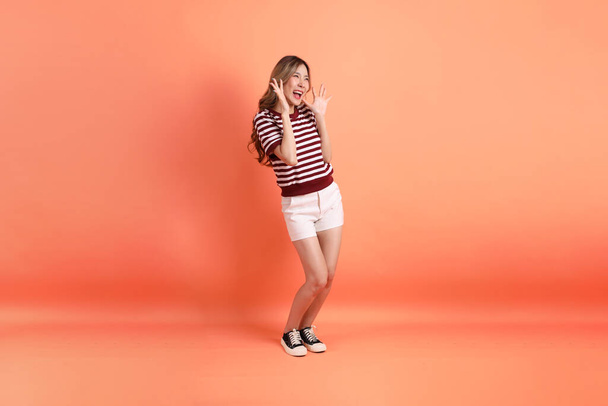 Η νεαρή Ασιάτισσα με τα καθημερινά της ρούχα, με μια χειρονομία έκπληξη στο πορτοκαλί φόντο.  - Φωτογραφία, εικόνα