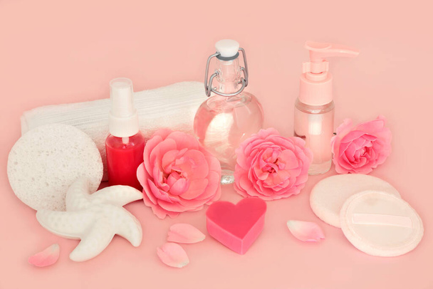 Rose bloem schoonheidsproducten op roze. Natuurlijke zuivere vrouwelijke gezondheid spa behandeling voor de gevoelige huid. Vrouwelijke ingrediënten met zeep, hydrateren, gel, aromatherapie olie en bloemen. - Foto, afbeelding