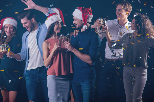 Счастливая группа людей, пьющих шампанское, веселящихся и улыбающихся во время празднования Нового года на темном дымном фоне
 - Фото, изображение