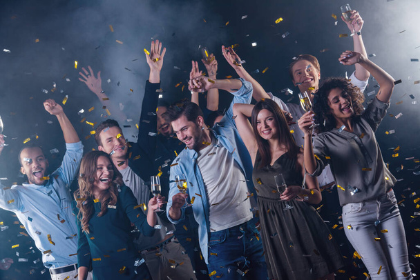 Happy group of people drinking champagne, dancing and smiling while celebrating New Year, on dark smoky background - Photo, Image