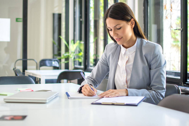 Önálló vállalkozó női vállalkozó jegyzetel, miközben irodai papírokkal dolgozik - Fotó, kép