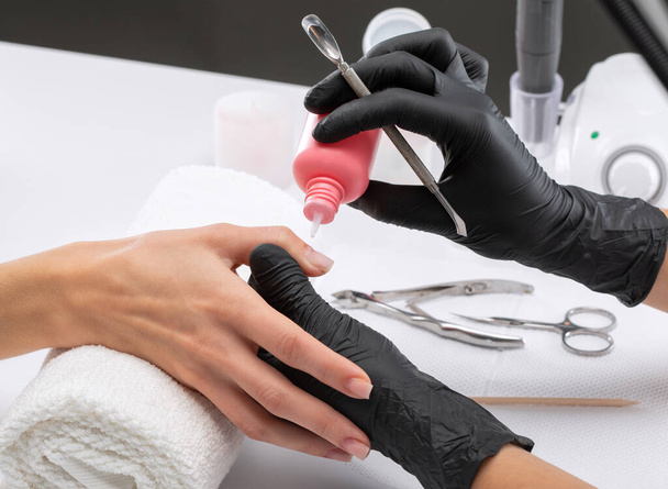 Manikiurzystka usuwa naskórek podczas zabiegu powiększenia paznokcia w salonie kosmetycznym. Profesjonalna pielęgnacja dłoni. - Zdjęcie, obraz