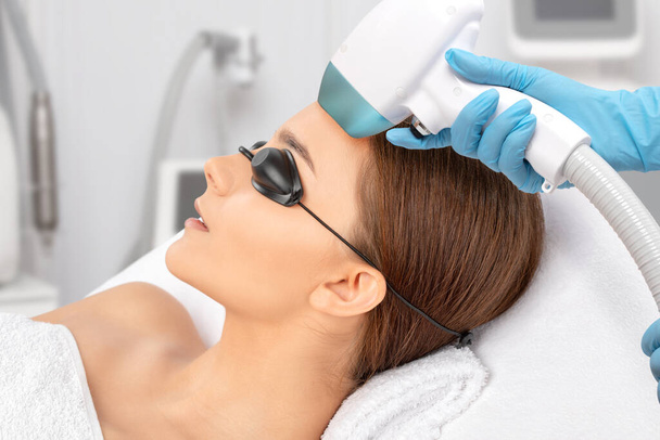 Epilation Haarentfernung auf dem Gesicht einer Frau. Kosmetikerin bei der Laserverjüngung in einem Schönheitssalon. Gesichtspflege. Hardware IPL Kosmetologie - Foto, Bild
