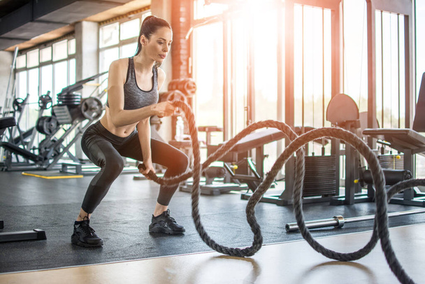 Mujer fitness haciendo ejercicio con cuerda de batalla en el gimnasio
. - Foto, Imagen