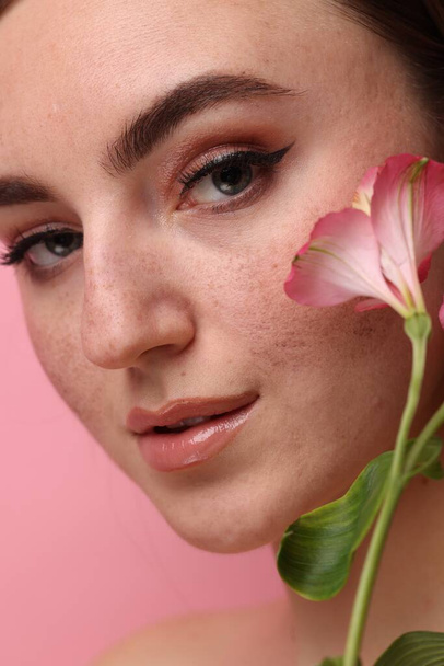 Beautiful woman with fake freckles and flower on pink background, closeup - Zdjęcie, obraz